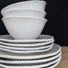 set of four white porcelain plates and bowls with an uneven rustic shape and beaded edging