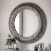 round wall mirror with a wide metal frame with a decorative filigree design finished in a pewter tone