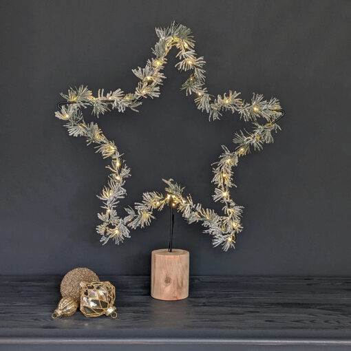 large black wire star on a rustic wooden base dressed with warm white LED lights and frosted faux pine sprigs