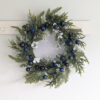 faux pine and mixed foliage wreath attached to a sturdy round twig base and adorned with navy blue baubles and iridescent glitter