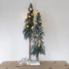 2 tall and slim nordic style faux christmas trees secured in a wooden base and dusted with snow