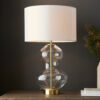 large glass table lamp with a clear hourglass silouette, satin brass accents and vintage white drum lampshade