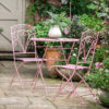 foldable metal bistro set including two chairs and a round table finished in pink with a decorative leaf cut-out design